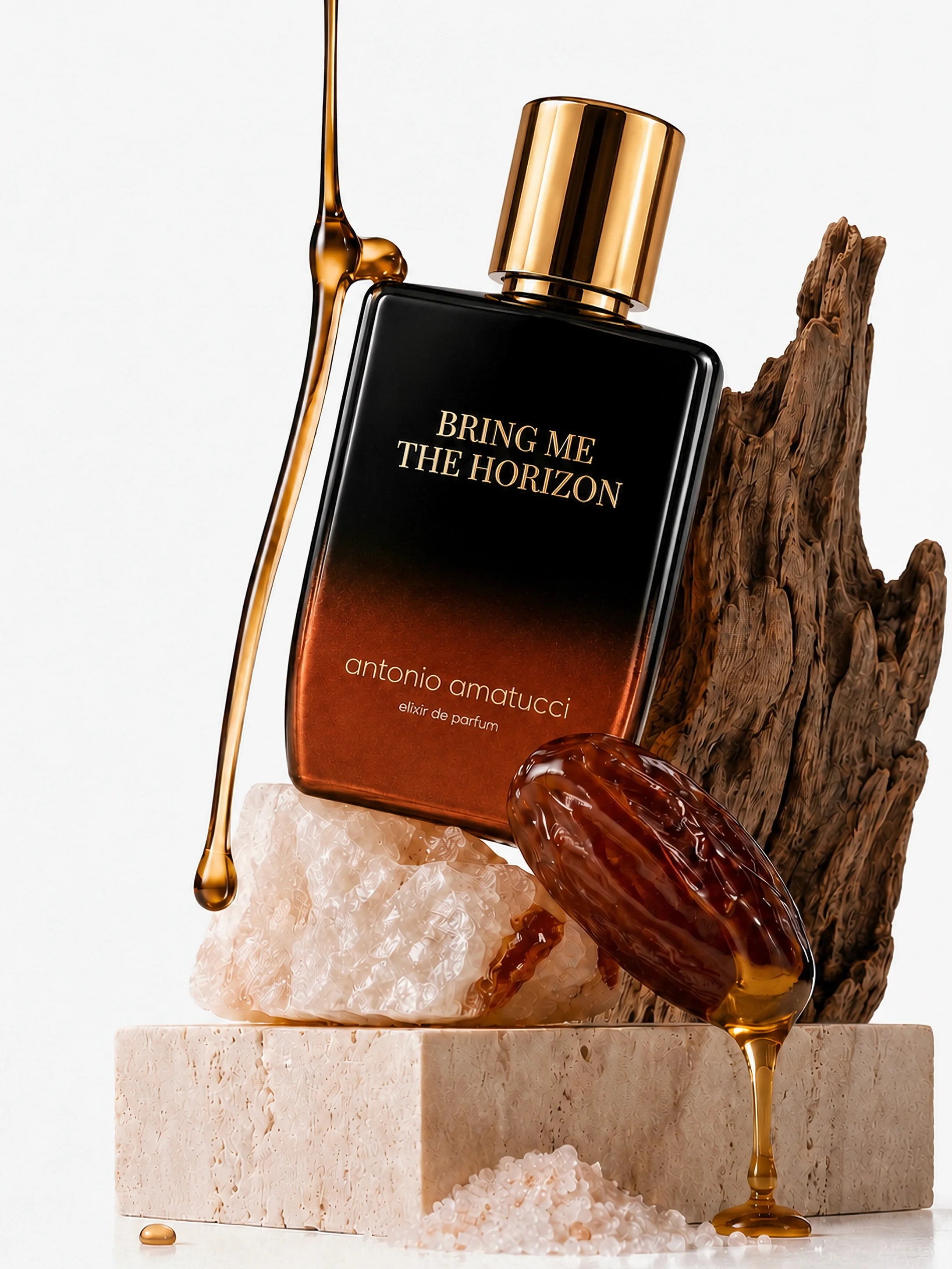 Bring Me The Horizon di Antonio Amatucci. La bottiglia di vetro sfumata dal nero al bronzo poggia su una roccia di sale rosa e un blocco di travertino, affiancata da un pezzo di legno antico e un dattero lucido da cui cola del miele dorato.